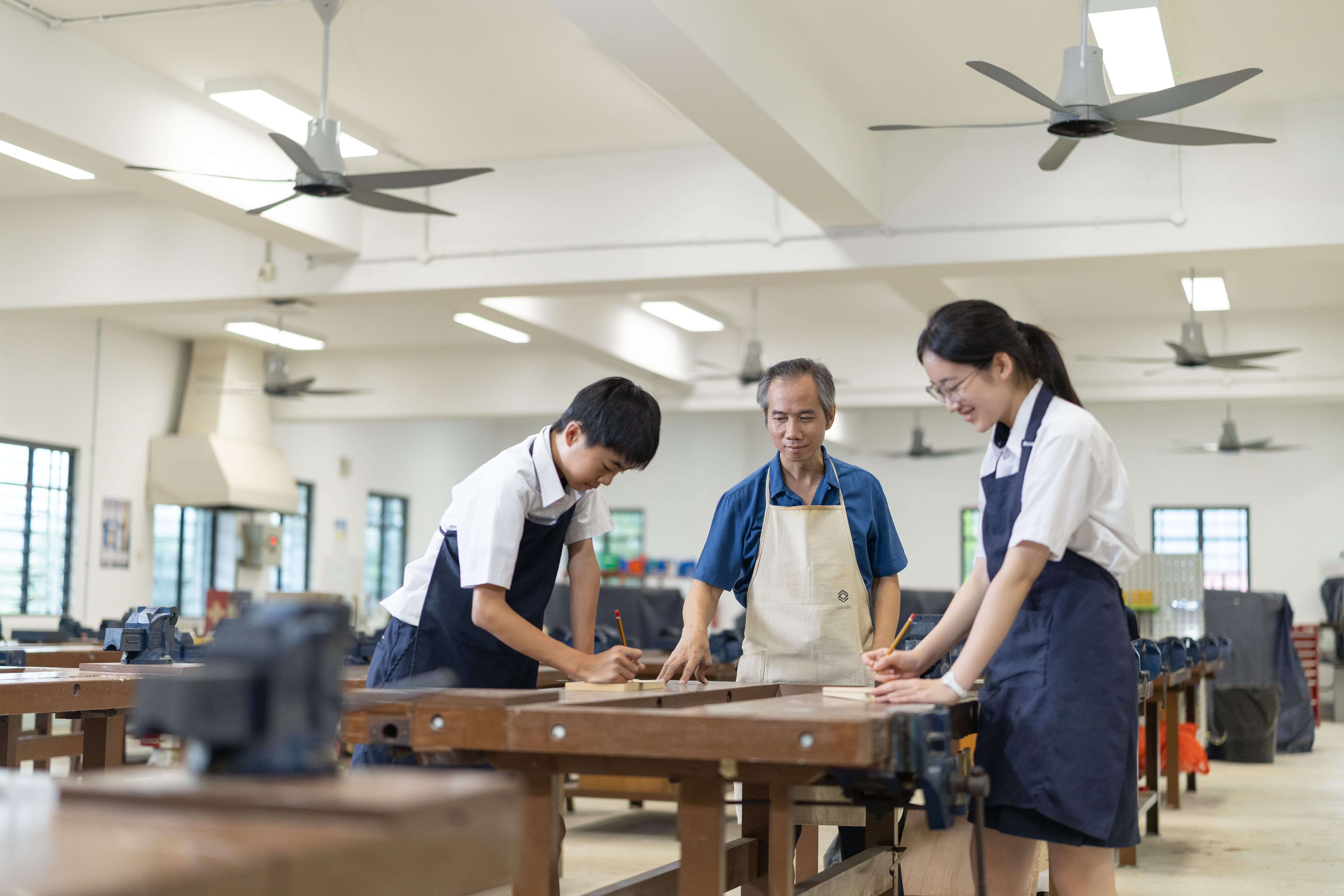 Teacher teaching 2 students how to design using wood.